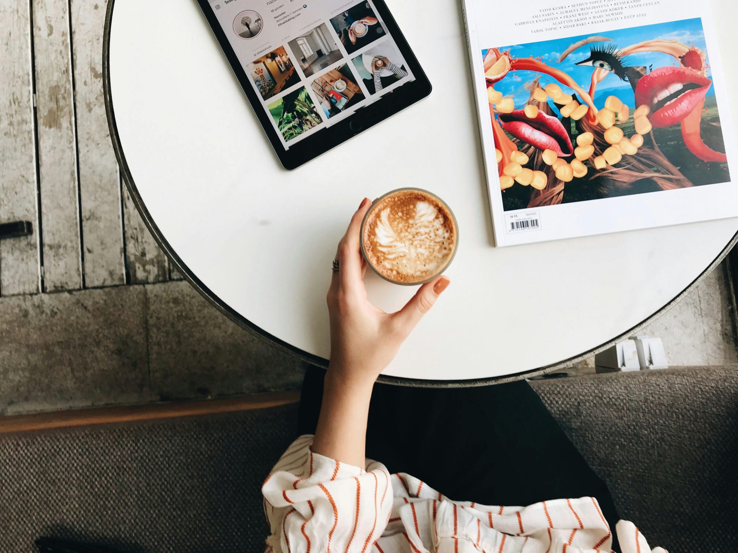Overhead view of a cozy coffee break with latte, tablet, and magazine on a stylish round table.